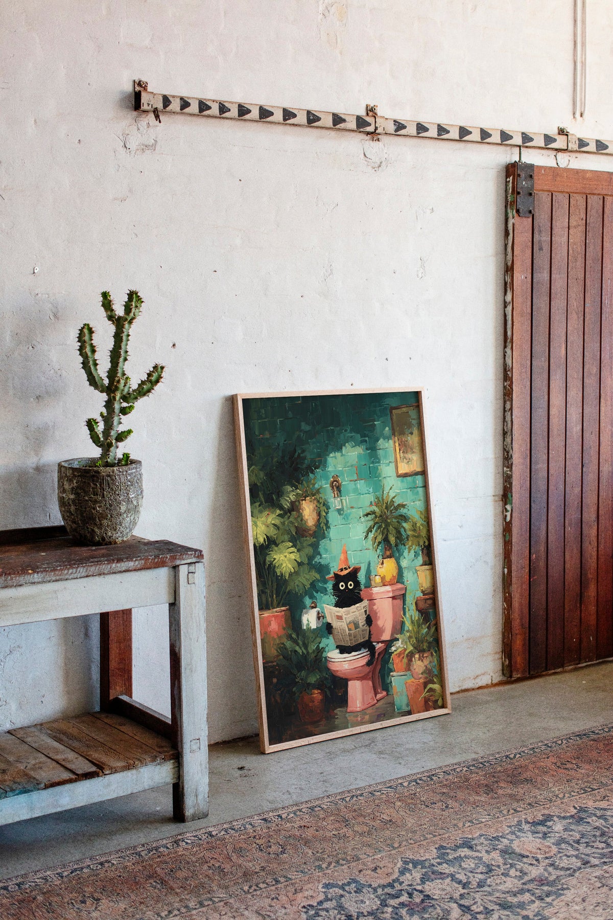 Framed cat artwork leaning on floor, teal brick background with potted plants and cactus