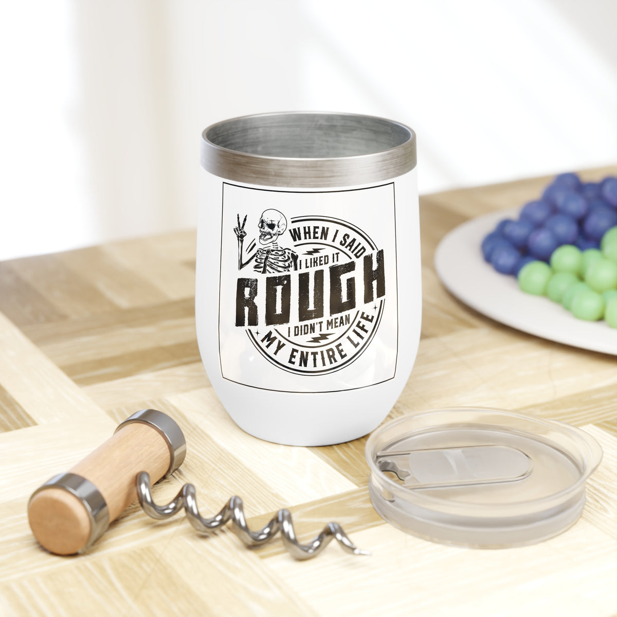 White wine tumbler with clear lid and skull quote graphic, shown on table.