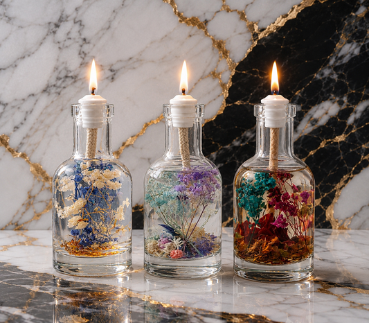 Three glass botanical oil candles in clear bottles with dried flowers and lit wicks