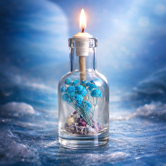 Neptune oil candle in clear glass bottle with blue dried flowers and lit wick