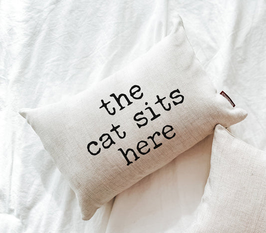 Off-white linen pillow embroidered 'the cat sits here' with stitched brand tag
